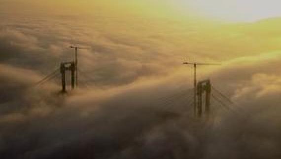 A ponte de Rande en obras e inmersa na néboa da ría no solpor.